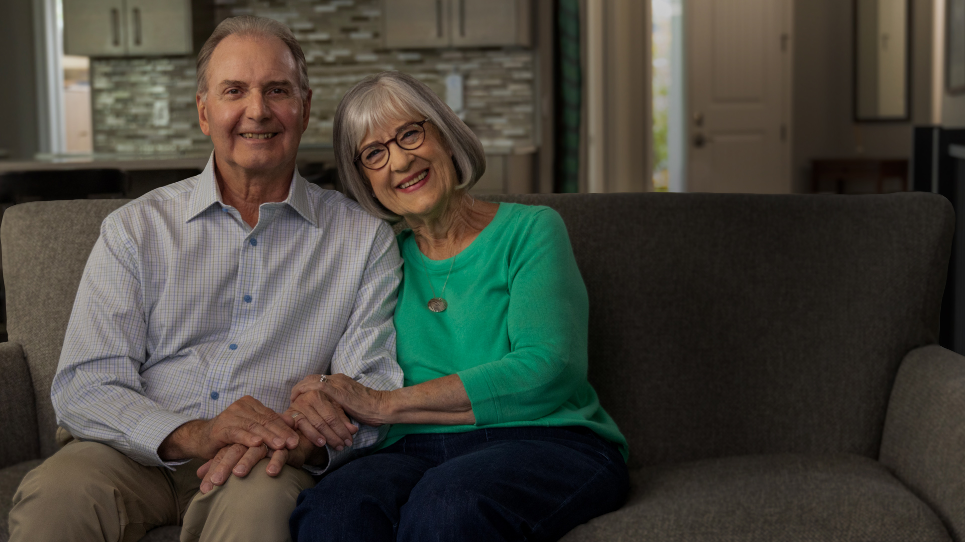 A patient story video of Mary, an adult female ABECMA® (idecabtagene vicleucel) patient, shown with glasses and short grey hair wearing a green long sleeve shirt while sitting on a couch with her arms crossed